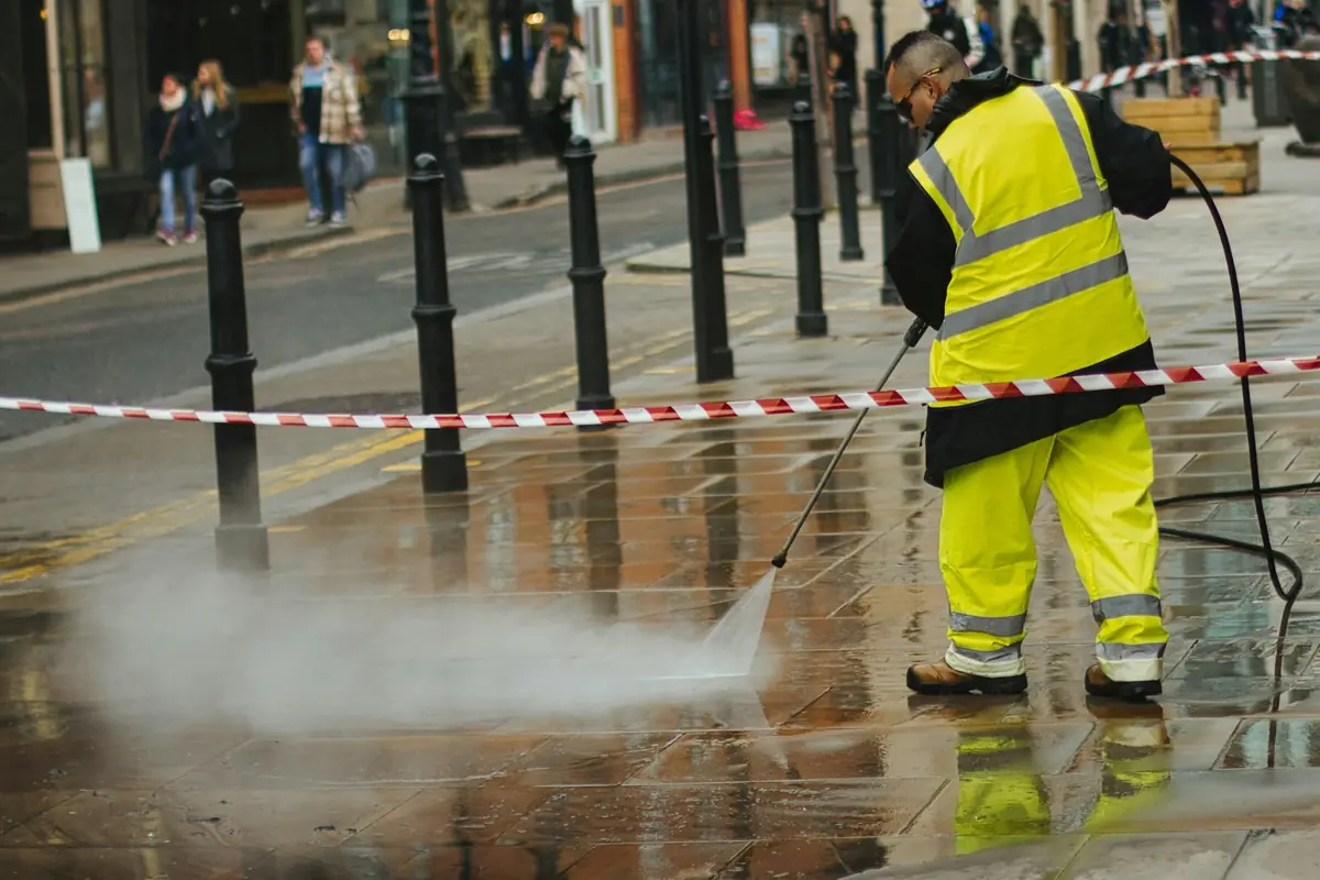 Worker using a pressure washer on pavement